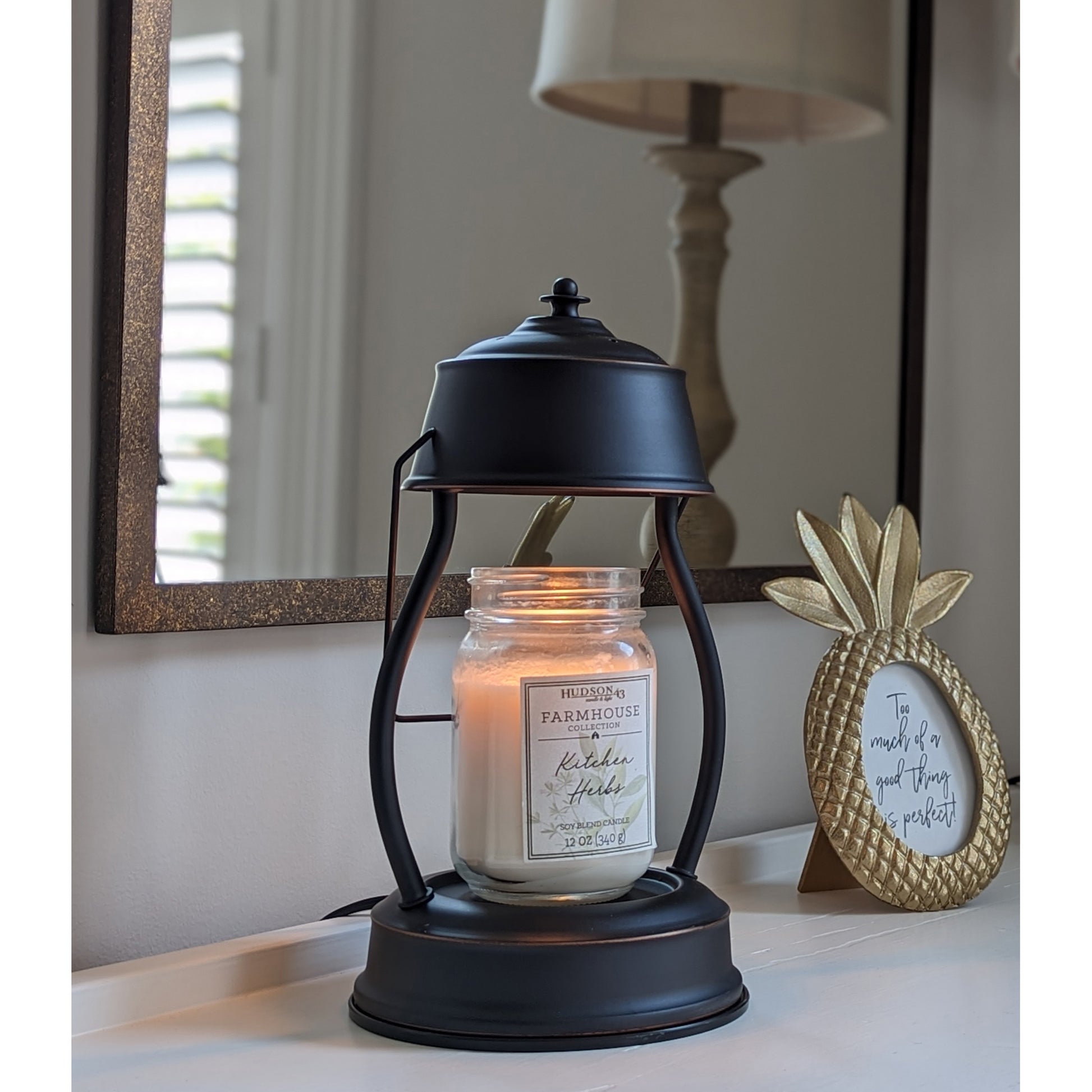 Image, lit rubbed bronze candle warmer with larger mason jar scented candle placed on an entry hall table.