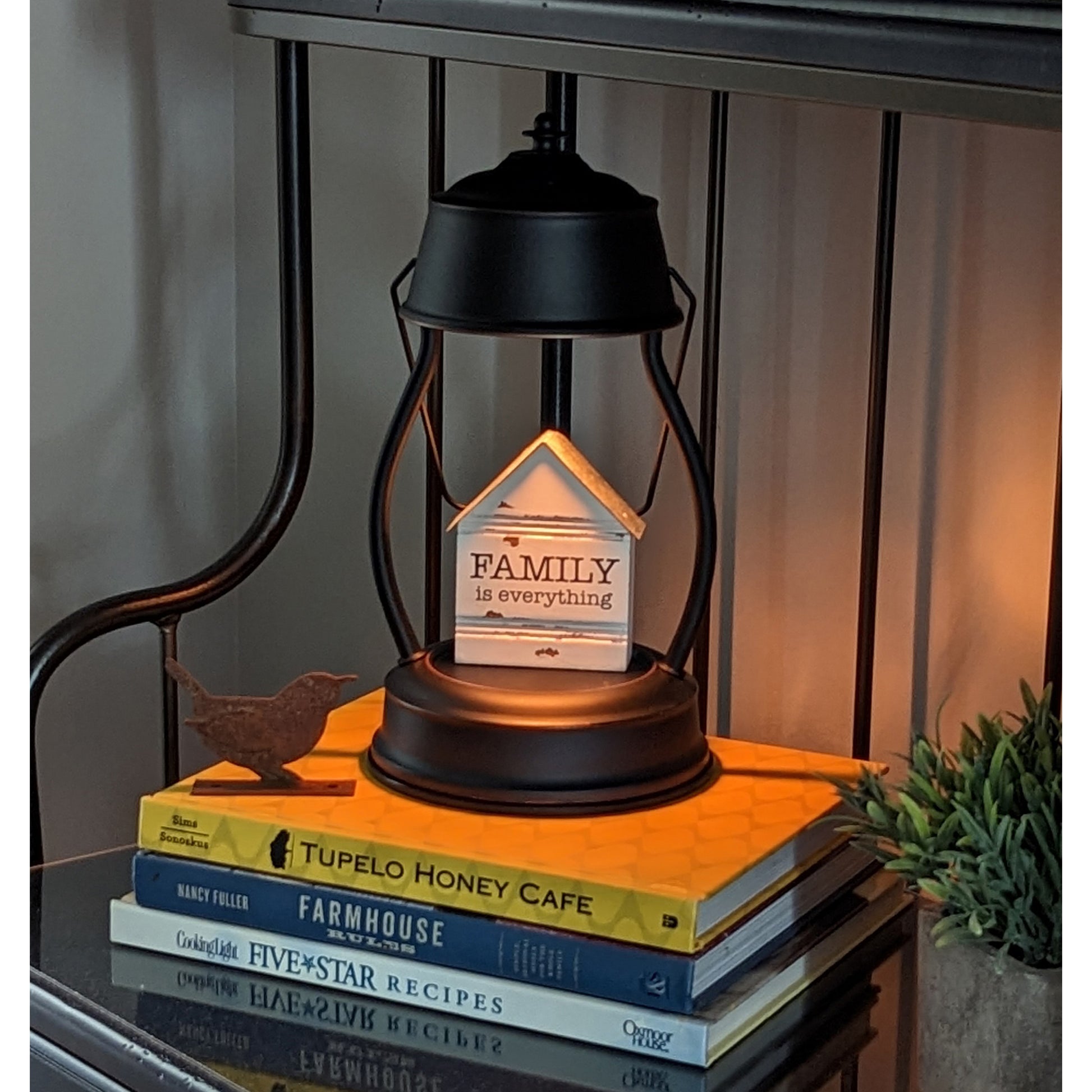 Image, lit rubbed bronze candle warmer with knickknack displayed placed on shelf on top of cookbooks.