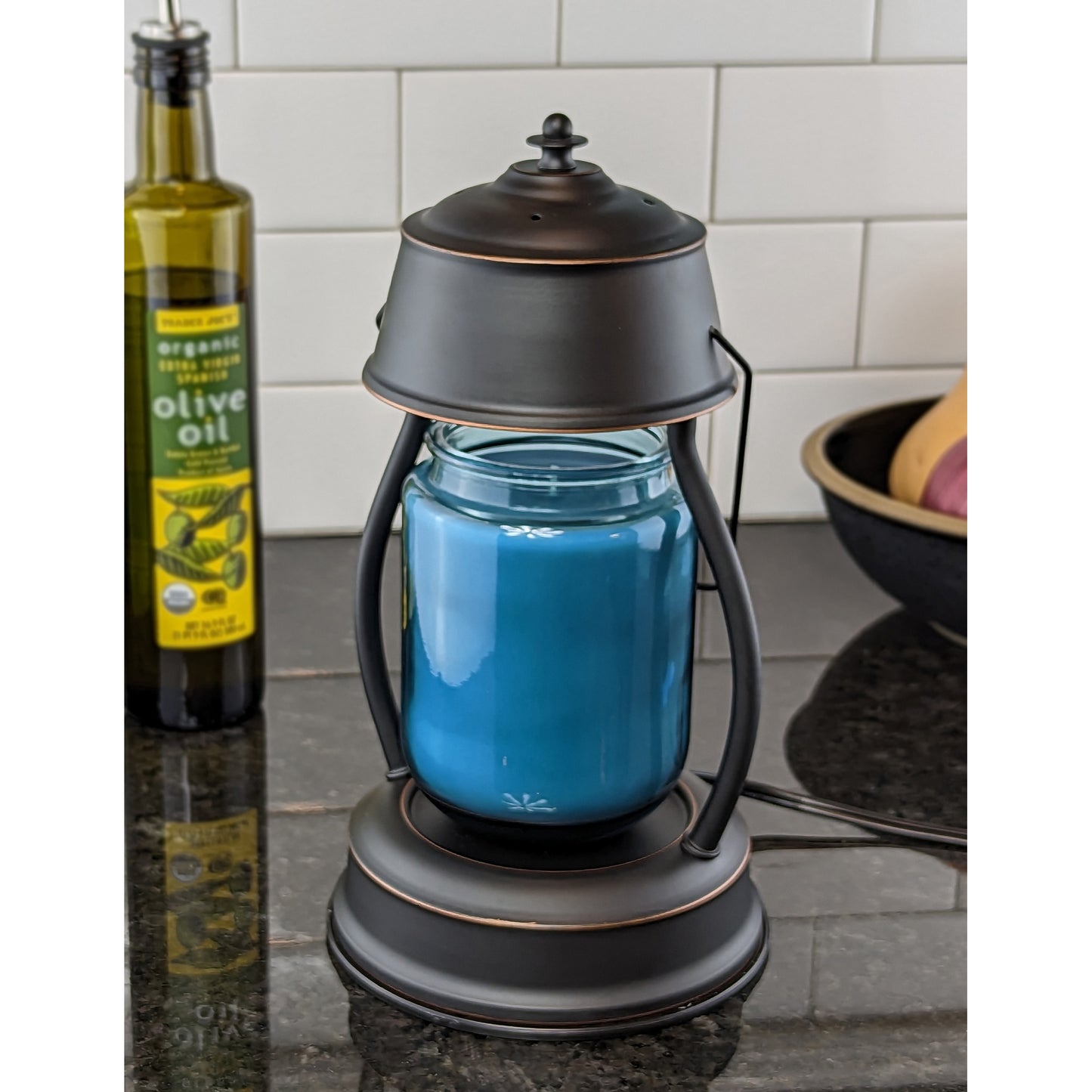 Image, rubbed bronze candle warmer with extra large scented candle on granite countertop in kitchen.