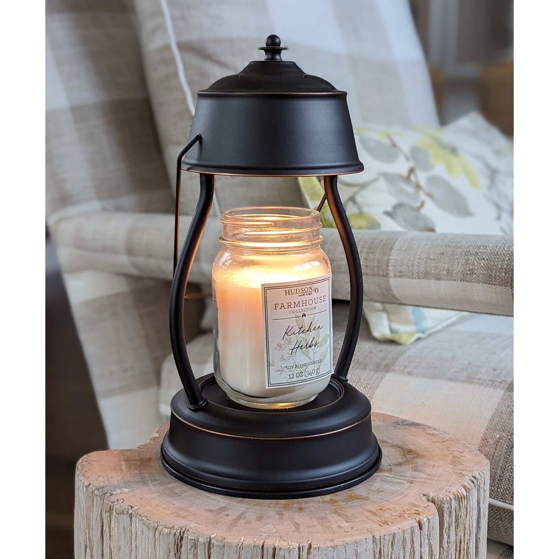 Image, lit rubbed bronze candle warmer with large mason jar scented candle sitting on a stone petrified log.