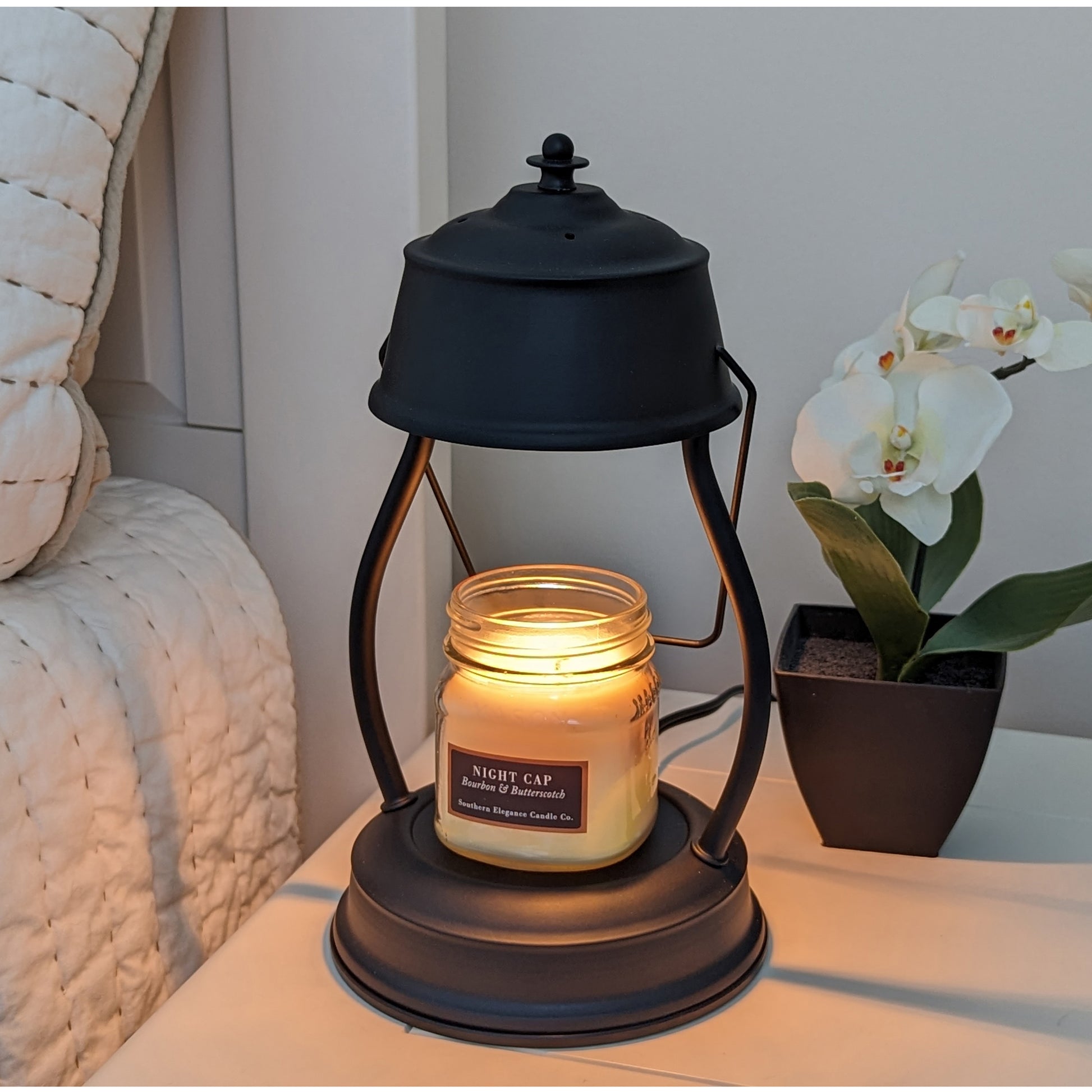 Image, lighted black candle warmer on a bedside table with small scented candle.