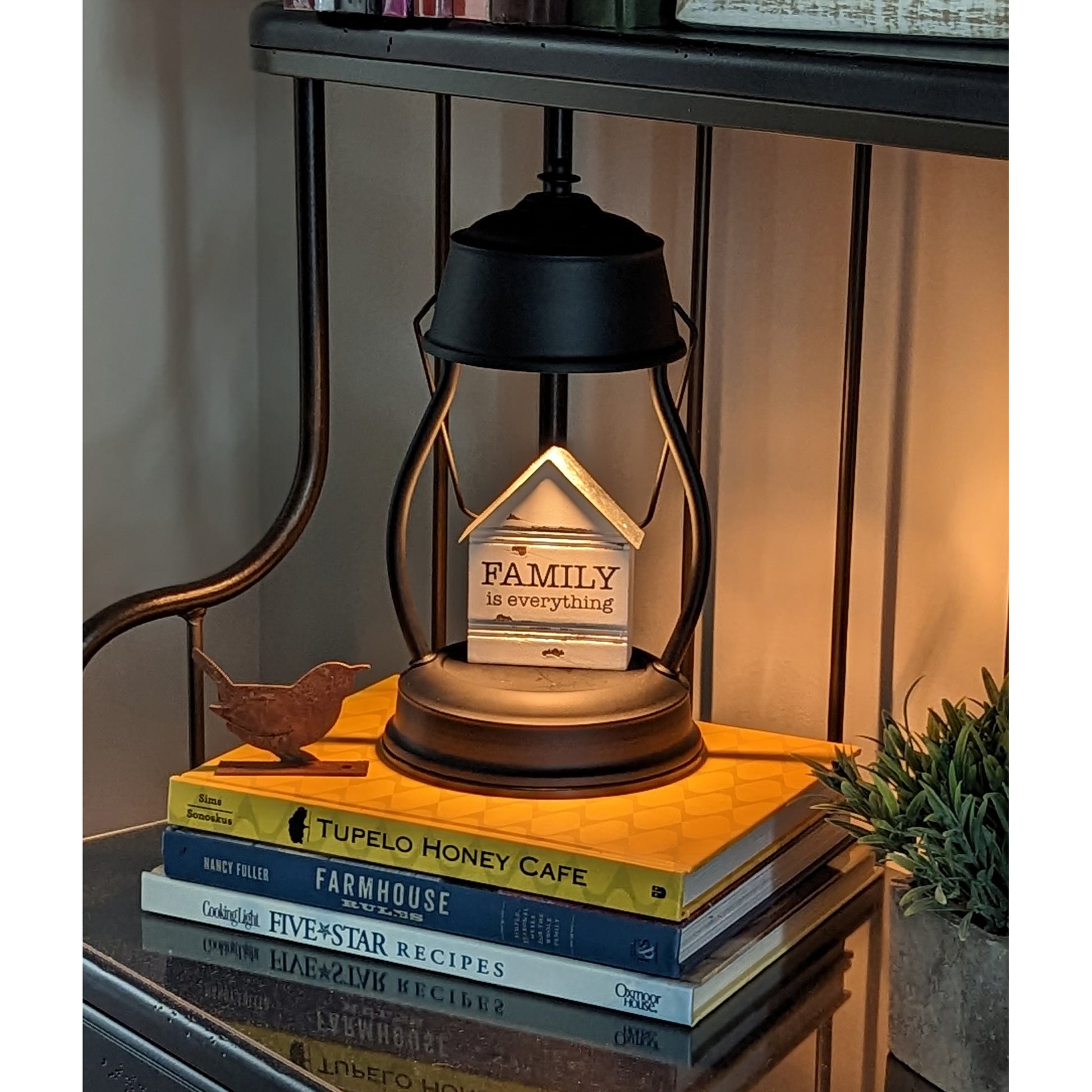 Image, lit black candle warmer with knickknack displayed placed on shelf on top of cookbooks.