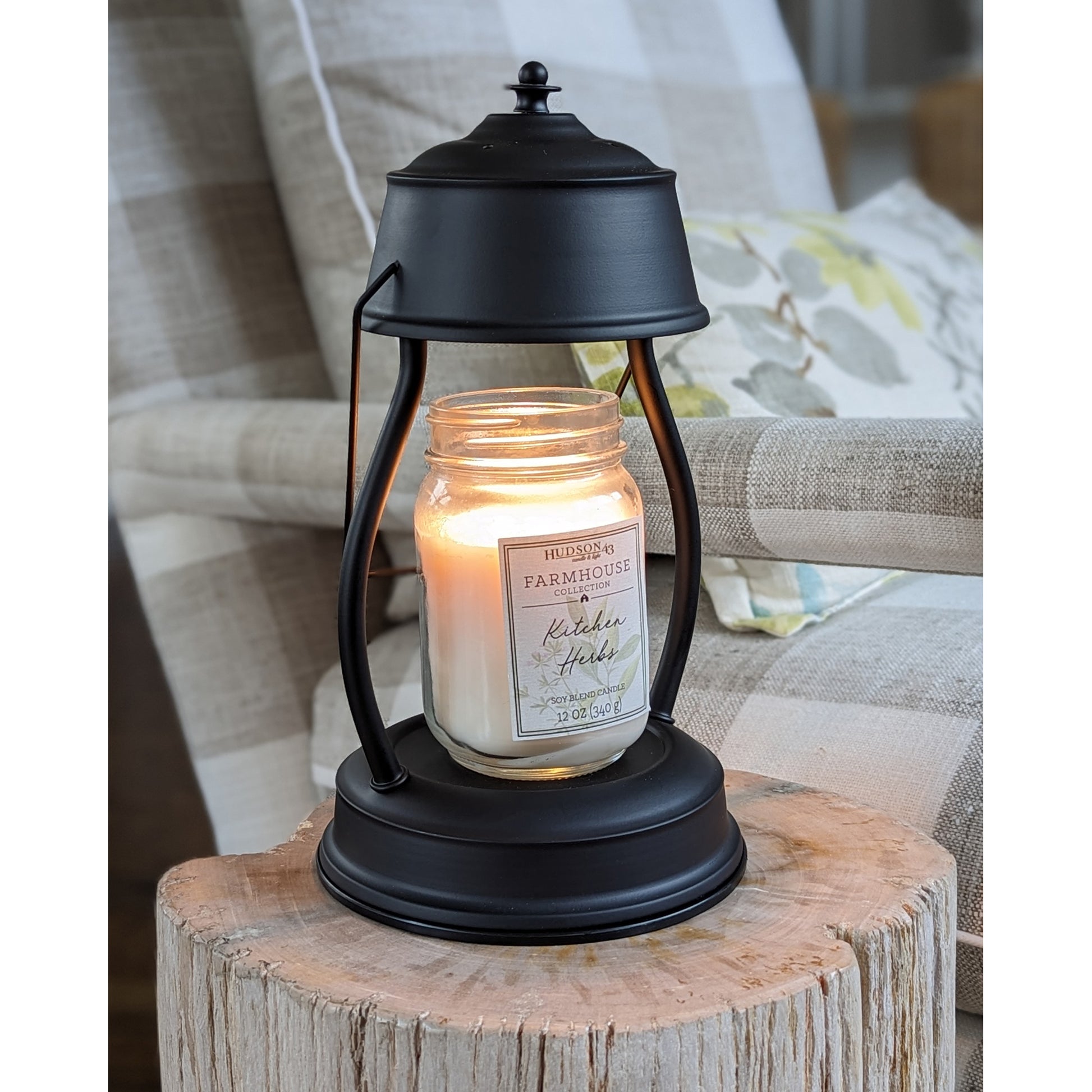 Image, lit black candle warmer with large mason jar scented candle sitting on a stone petrified log.