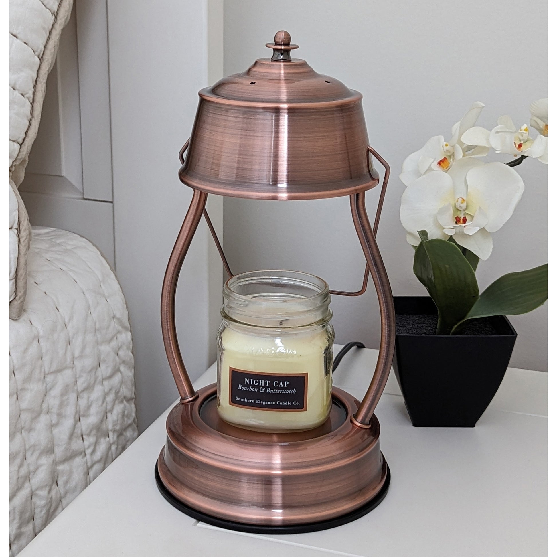 Image, unlit copper candle warmer on a bedside table with small scented candle.