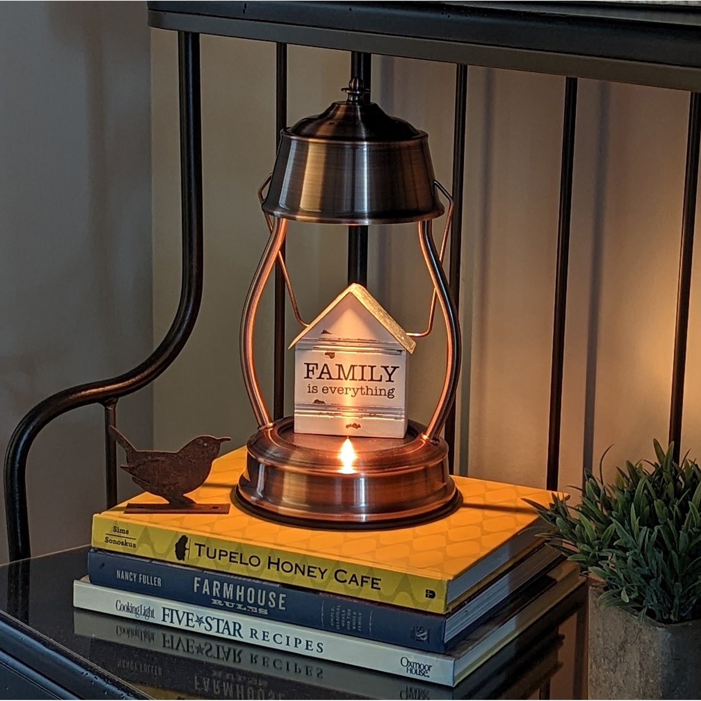 Image, lit copper candle warmer with knickknack displayed placed on shelf on top of cookbooks.
