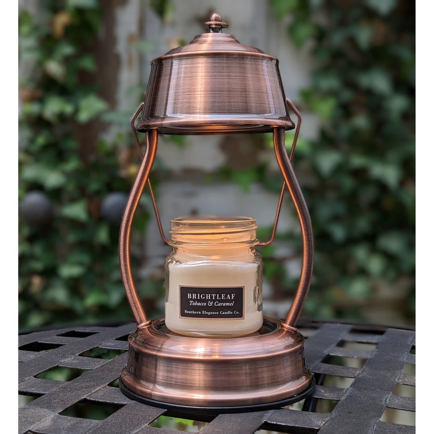 Image, lit copper candle warmer on outdoor wrought iron table.