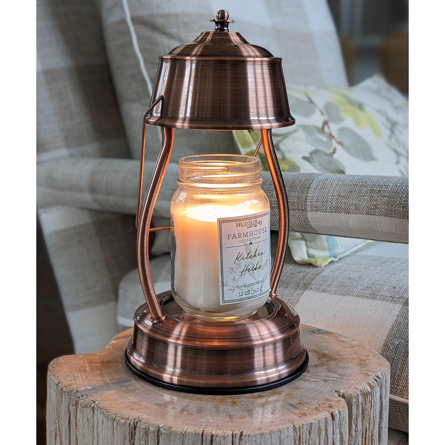 Image, lit copper candle warmer with large mason jar scented candle sitting on a stone petrified log.